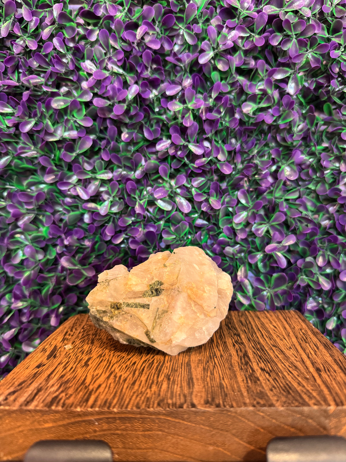 Wider view of the raw quartz chunk showing green tourmaline inclusions on a wooden stand.