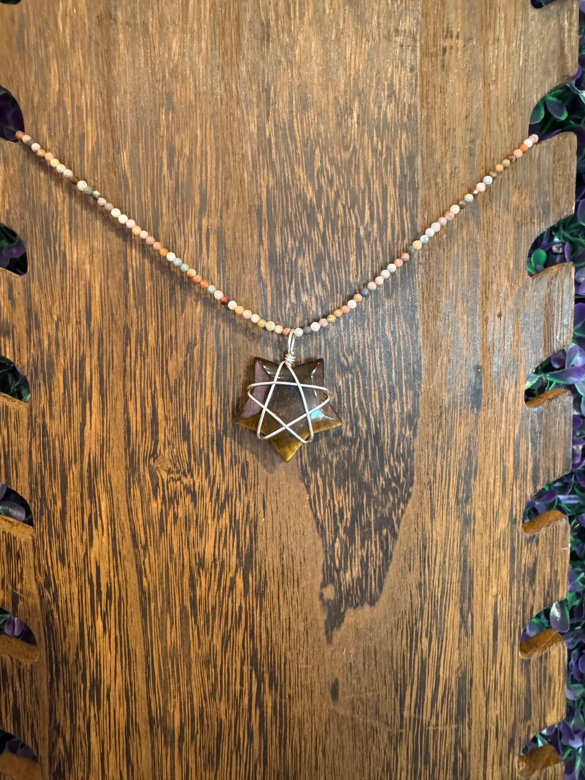 Tiger's eye star necklace hanging against dark wood.