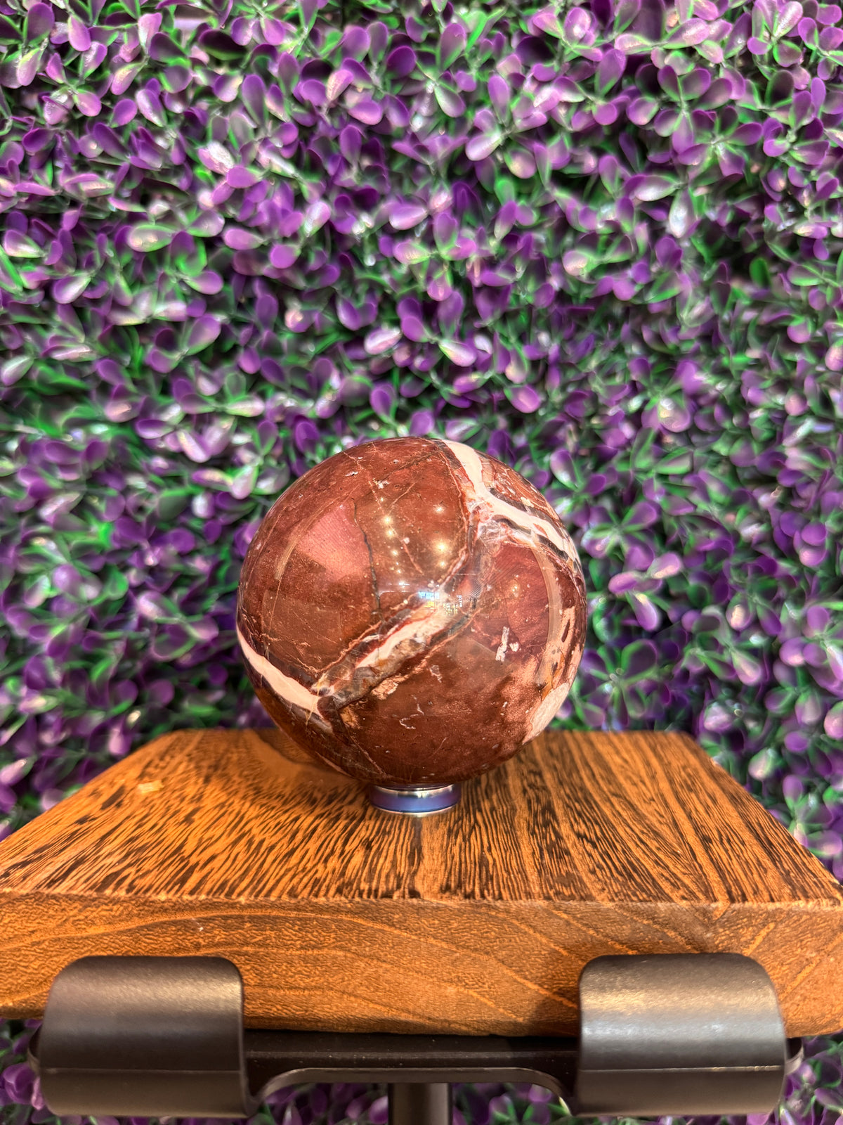 Polished deep red brecciated red jasper sphere with white veins on a wooden stand.