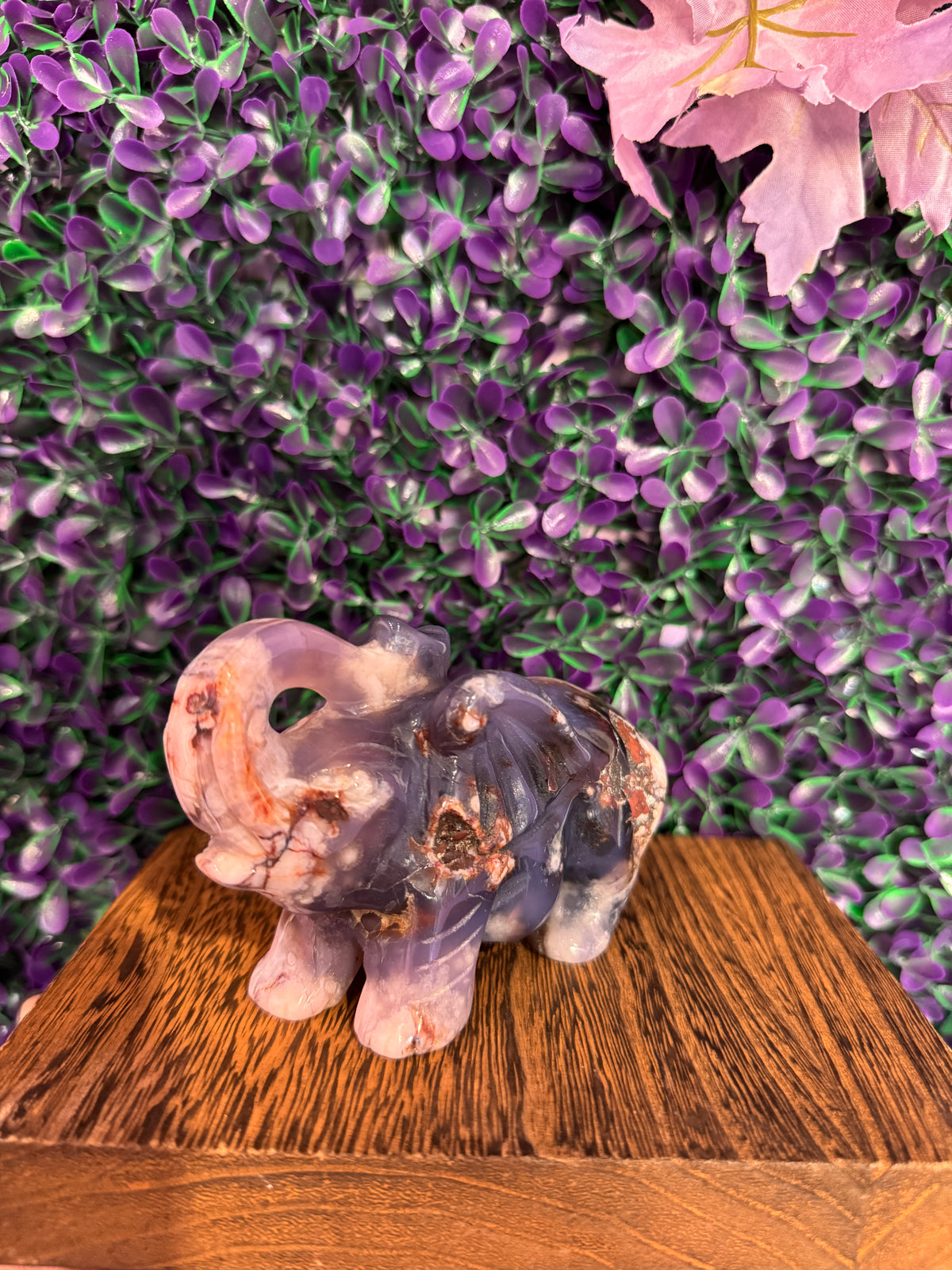 Side profile of a lavender flower agate elephant carving on a wood block.