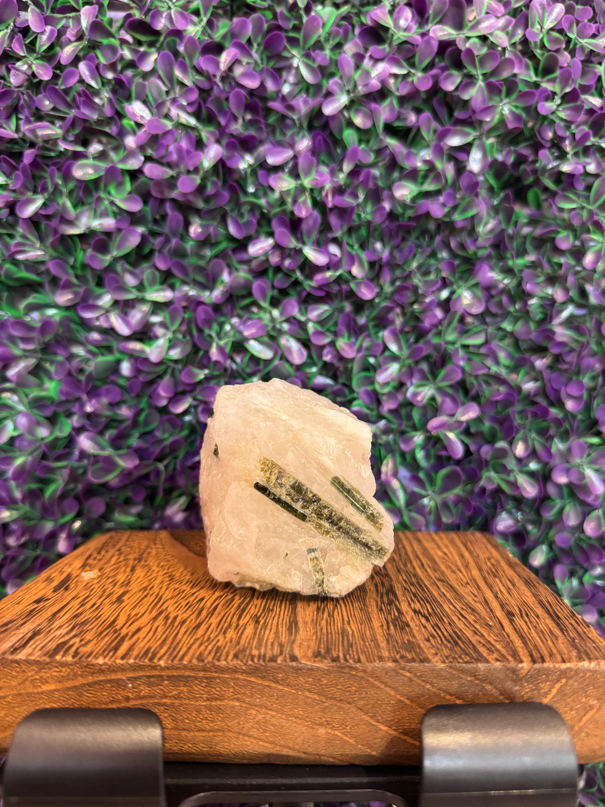 Raw milky quartz specimen with prominent dark green tourmaline rods across the face, on a wooden stand.