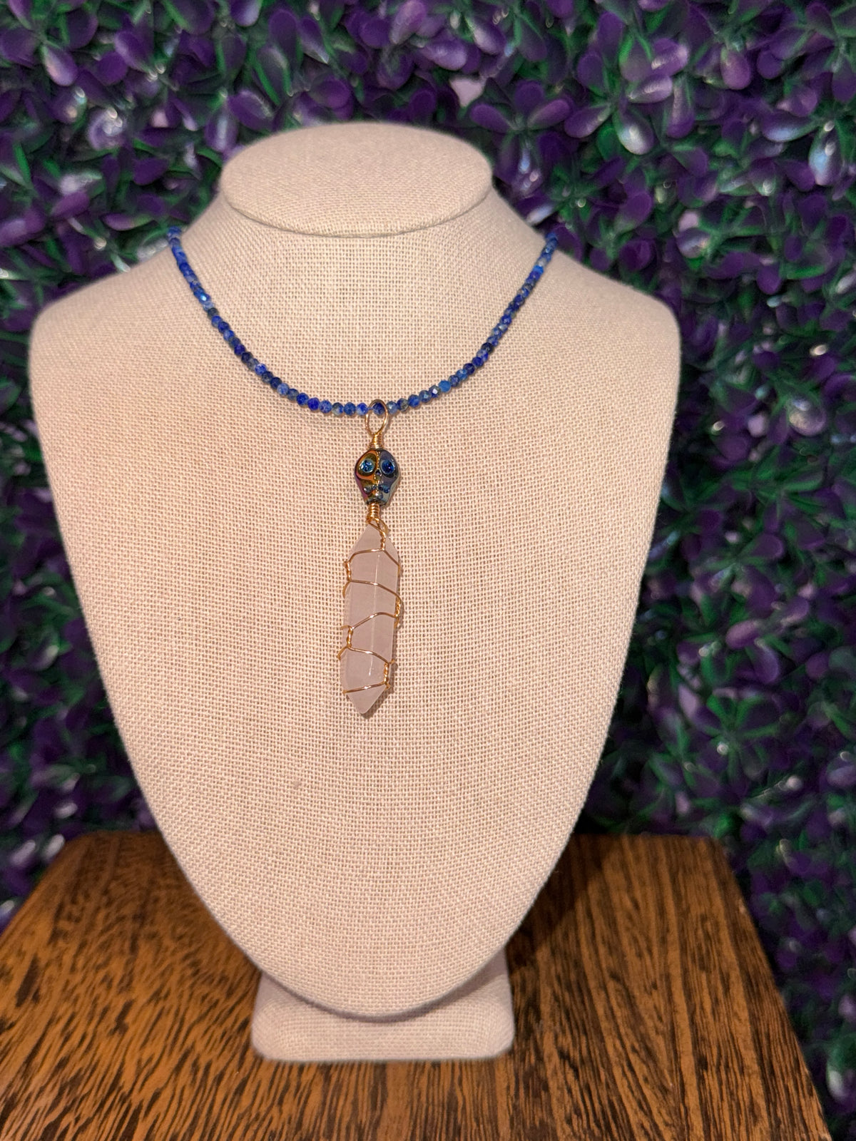 Pink Point and Skull Bead Necklace — product photo 1. A pale pink point wrapped in gold-tone wire, accented with a blue-and-gold skull bead and a blue faceted bead chain.