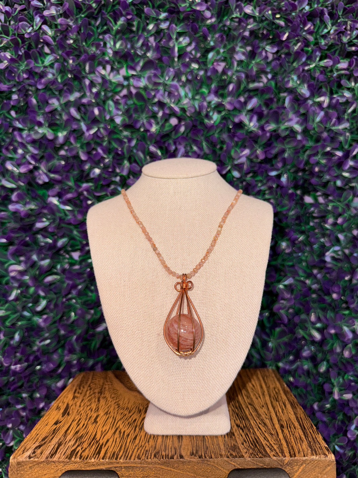 Pink Swirl Sphere Cage Necklace — product photo 1. A pink sphere with white swirling bands, held in a copper-tone teardrop wire cage on a peach faceted bead chain.