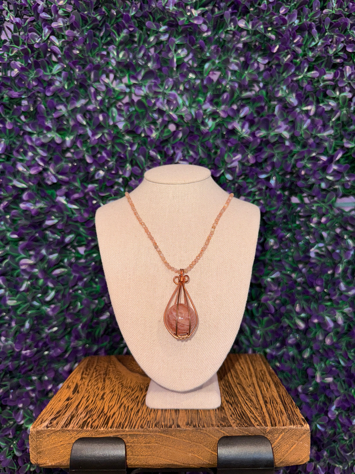 Pink Swirl Sphere Cage Necklace — product photo 2. A pink sphere with white swirling bands, held in a copper-tone teardrop wire cage on a peach faceted bead chain.