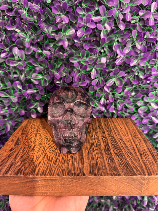 Purple-Gray Speckled Skull Carving — product photo 1. A polished skull carving with dark purple-gray coloring and pink-red speckles.