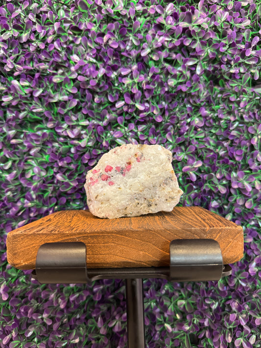 Ruby in marble specimen on a stand showing pink-red crystals in white matrix.