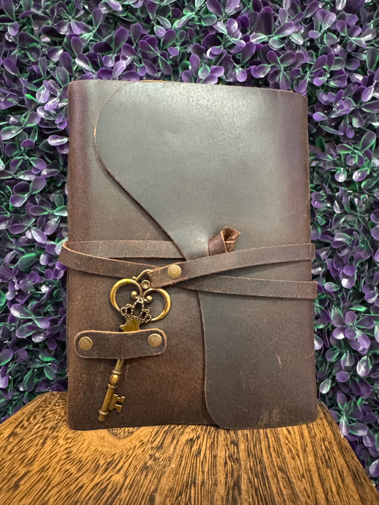 Dark brown wrap journal with a leather-style tie strap and a brass-tone skeleton key charm.