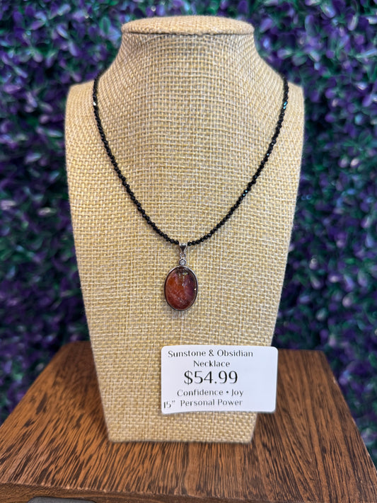 Oval sunstone pendant in a silver-tone bezel on a black obsidian bead strand, with a tag reading Sunstone & Obsidian Necklace $54.99.