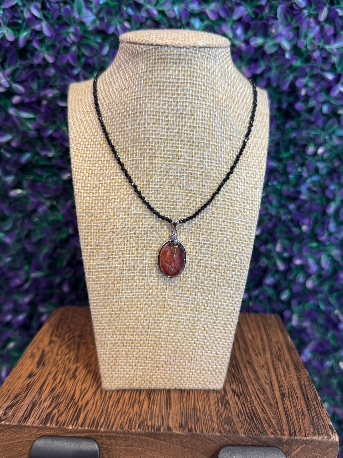 Sunstone and obsidian necklace on a burlap bust showing the red-orange oval pendant.