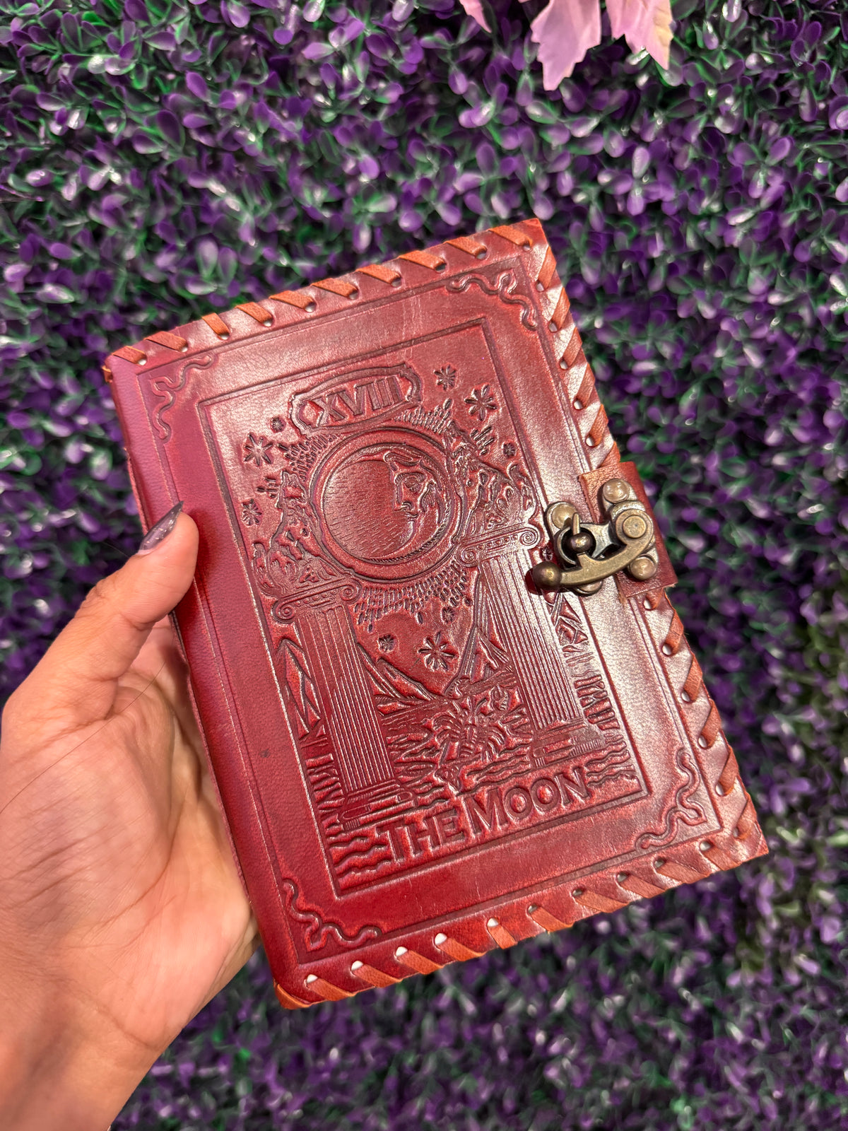 Hand holding The Moon tarot journal showing the XVIII card cover.