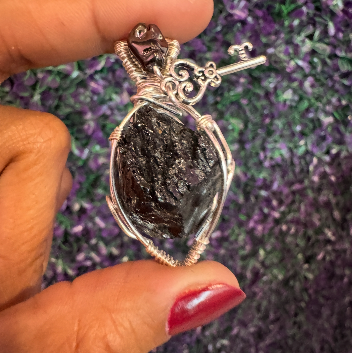 Close-up of a dark rough tourmaline pendant in silver-tone wire wrap with a small key charm.