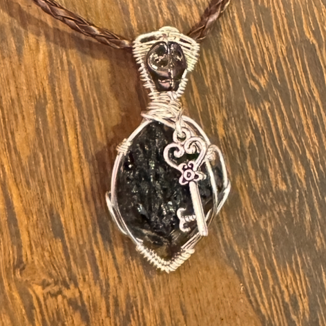 Full view of a wire-wrapped dark tourmaline key necklace on a brown cord displayed on a wood bust.